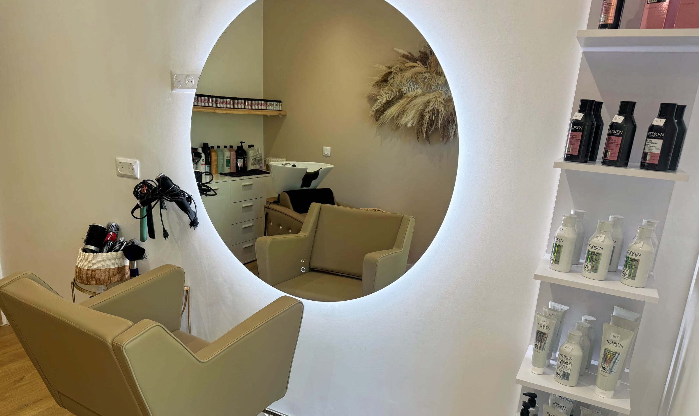 Deux fauteuils du salon reflétés dans le miroir rond, étagère de soins Redken